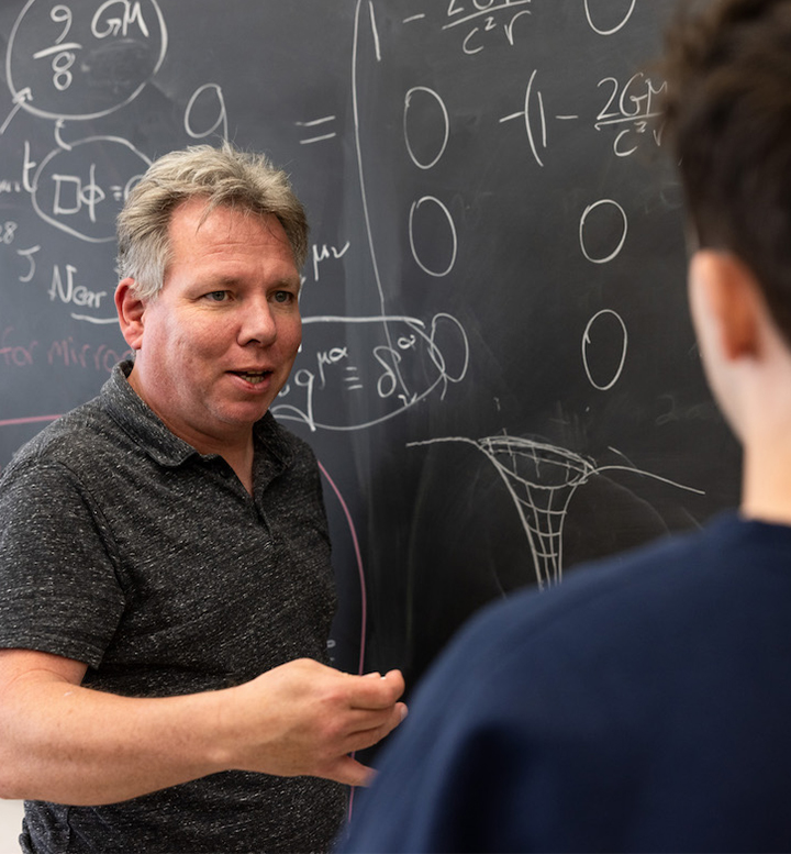 LMU Professor Jonas Mureika with student next to blackboard