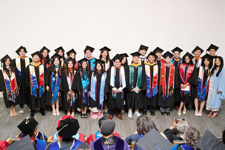 A large group of graduates standing at the front of a large auditorium of family and friends