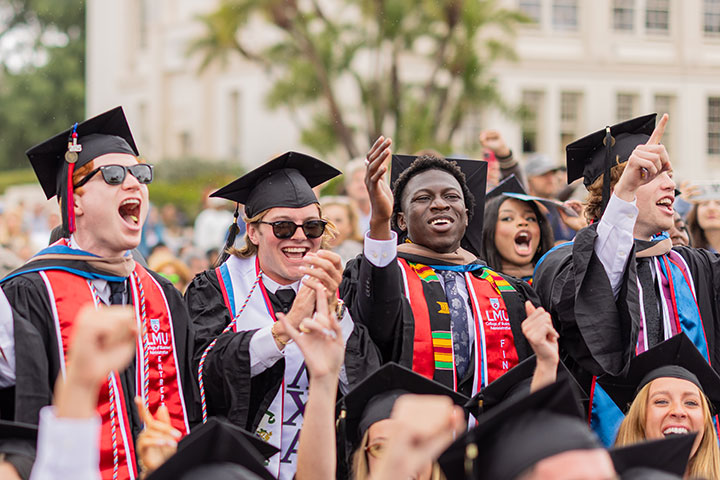 A group of graduates excitedly standing up at their chairs and cheering during commencement