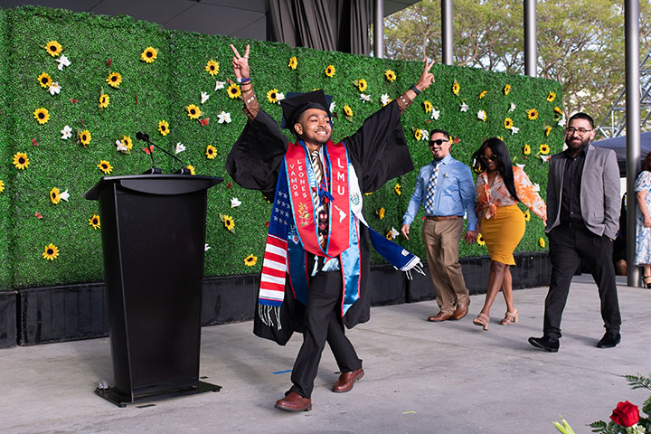 A graduate holding up peace signs at the audience as they cross the stage during Dia de Reconocimiento